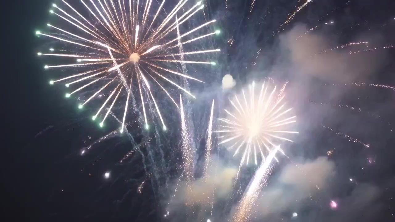 Gusci di crisantemo che esplodono riempiendo il cielo notturno durante i lanci, inviando scie di comete e fumo.