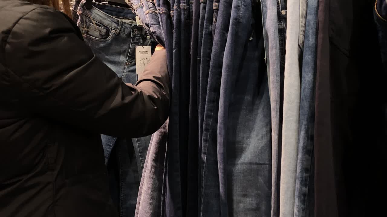 The girl checks the size of the pants on the tag. A clothing store with pants.