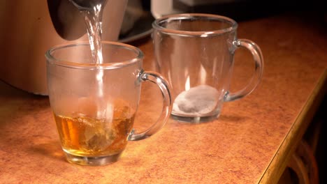 pouring boiling hot water over tea bags into a see through teacups