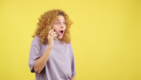 a young woman with curly hair looks shocked while on a phone call.