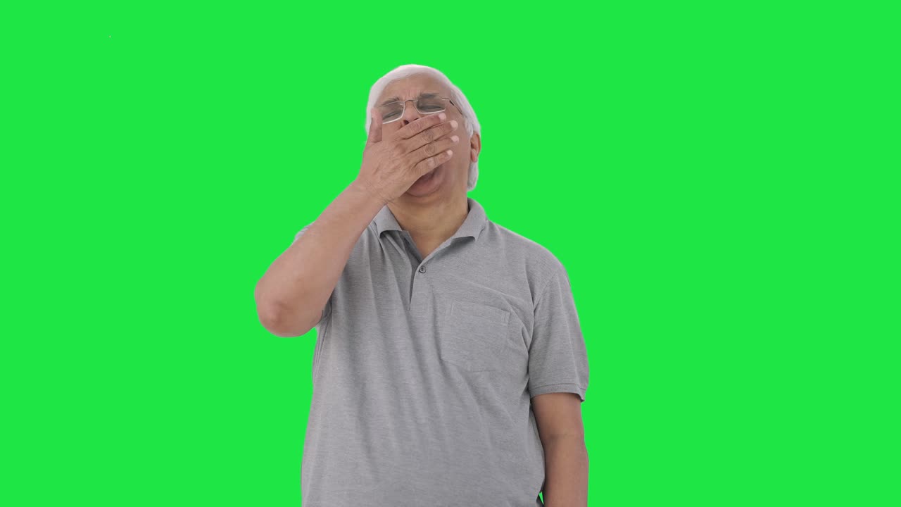 Anziano indiano assonnato e stanco che sbadiglia. Green screen.