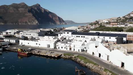 Verlassene-Weiße-Gebäude-In-Der-Nähe-Des-Hafens-Von-Hout-Bay-In-Südafrika-Mit-Chapman&#39;s-Peak-Und-Wohnhäusern-Im-Hintergrund