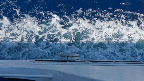 view from the side of a ship sailing through the water of a calm sea at midday