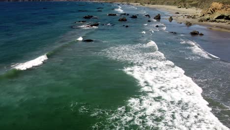 waves coming in on a sandy beach with rocks