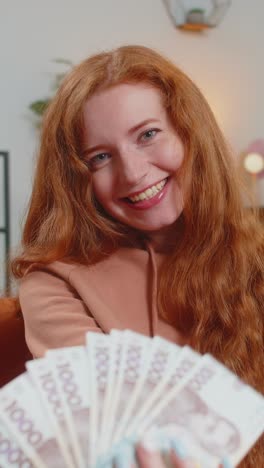 successful rich young caucasian woman holding euro bill money fan sitting on sofa couch at home