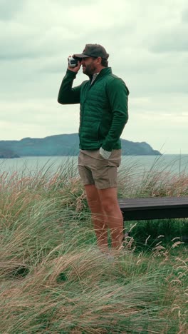 vertical shot of male golfer standing in rough using range finder to get accurate yardage to pin on coastal ireland links golf course on windy day