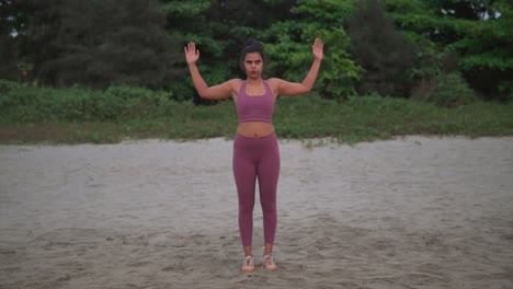 Woman-meditates-in-yoga-pose-on-sand-with-forest-in-background,-finding-inner-peace-through-breath-and-nature