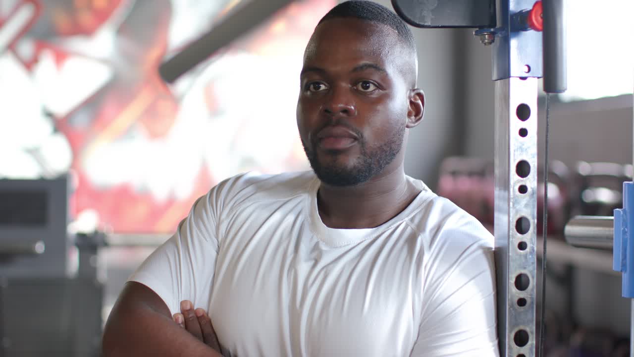 Hearing off-camera voice, African American adult man leaning in gym by squat rack, shifting gaze