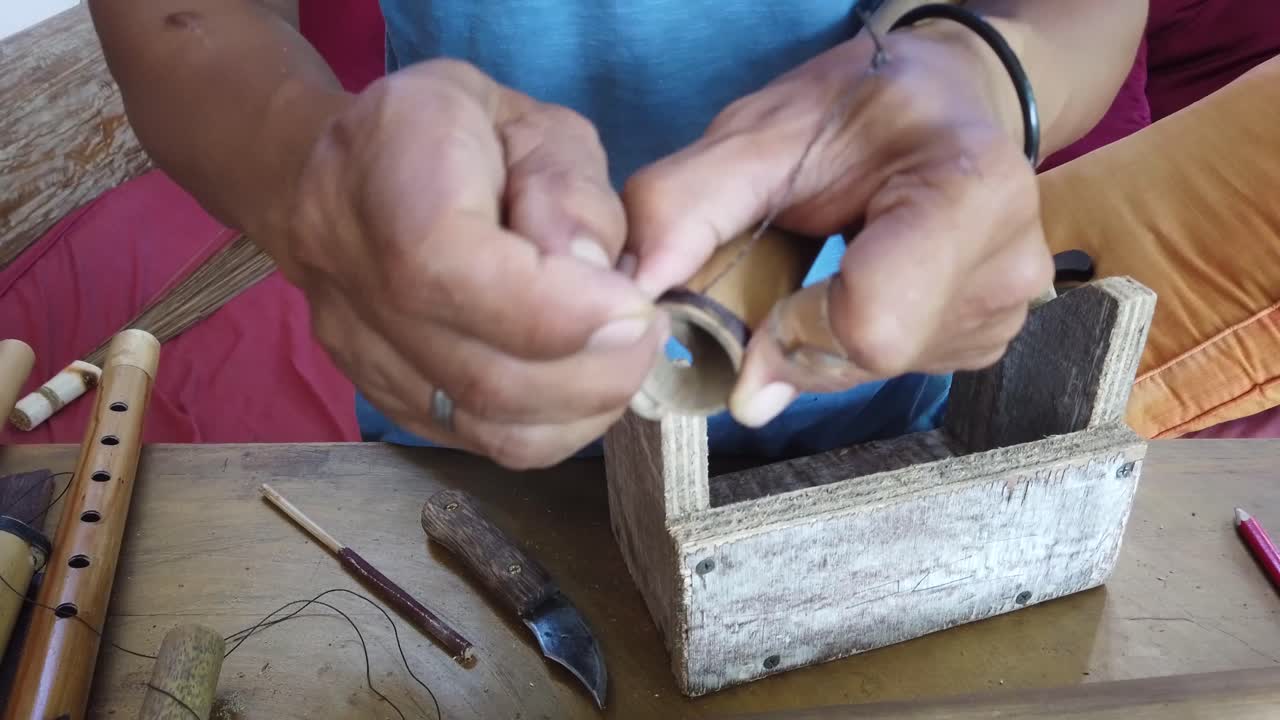 artesano hace una flauta musical tradicional de bambú manos de cerca atando una banda de rodadura de madera instrumento tradicional de indonesia