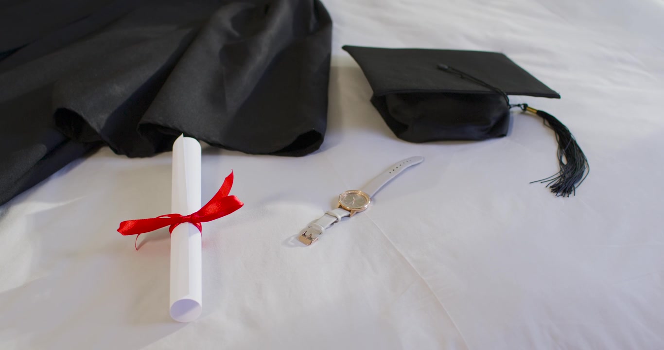 Camera starting to record is showing rolled diploma arranged on white bed as graduation display