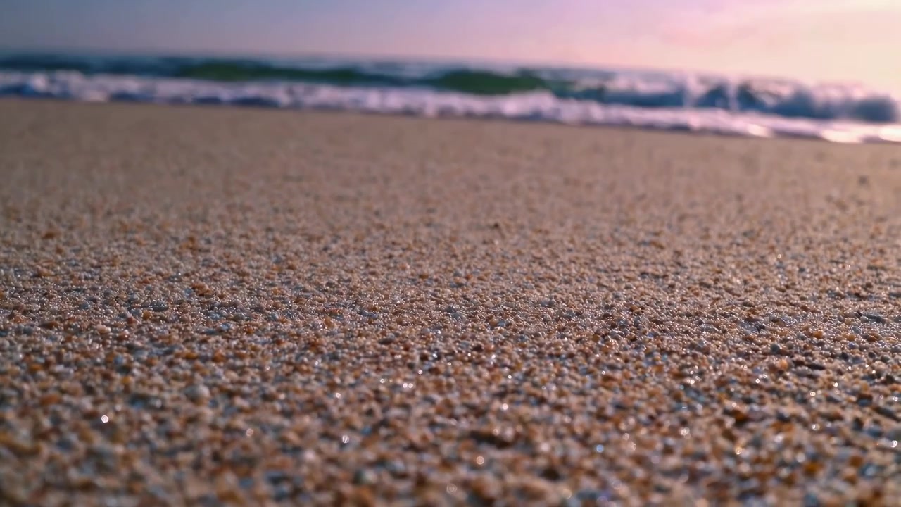 Nærbillede af sandstrand med blide havbølger ved solnedgang.