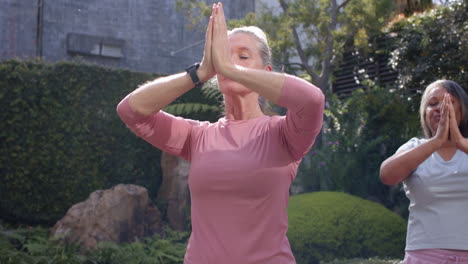 practicing yoga, multiracial female friends meditating outdoors in peaceful garden setting
