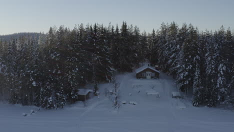 La-Vista-Ascendente-Aérea-Revela-Una-Remota-Cabaña-De-Bosques-Cubiertos-De-Nieve-En-Invierno-Entre-árboles-Alpinos-Al-Amanecer.