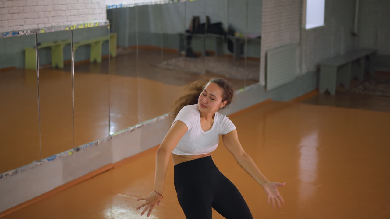 Woman in casual wear white top and black leggings flipping herself in fitness studio, showing energetic movement, athletic strength, balance, and control during workout