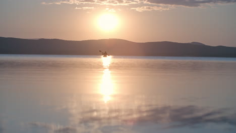 vista lejana de un hombre con gorra y chaleco salvavidas remando en una canoa en el lago al atardecer