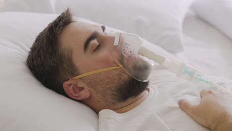 sick man lying on bed taking his oxygen mask off and coughing