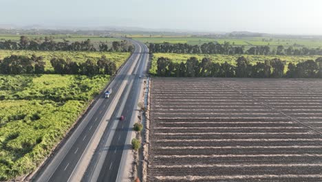 toma aérea cinematográfica de arriba hacia abajo siguiendo a un automóvil en la carretera peruana de varios carriles de panamericana norte entre vastas tierras de cultivo en ambas esquinas