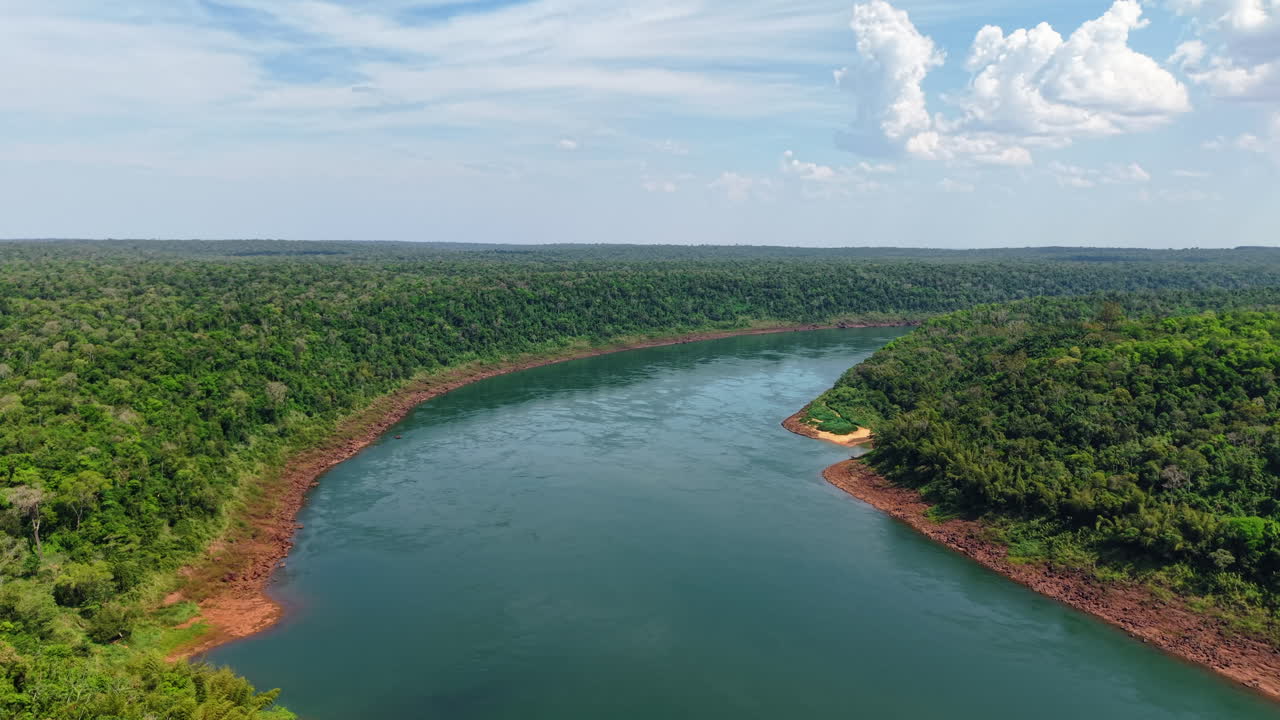Left hover drone captures vibrant color contrast between river, red soil, and jungle stretching to the horizon. Sunny day