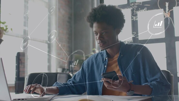 Mid adult man using phone and laptop in loft, incoming data animating analytics overlaying screen