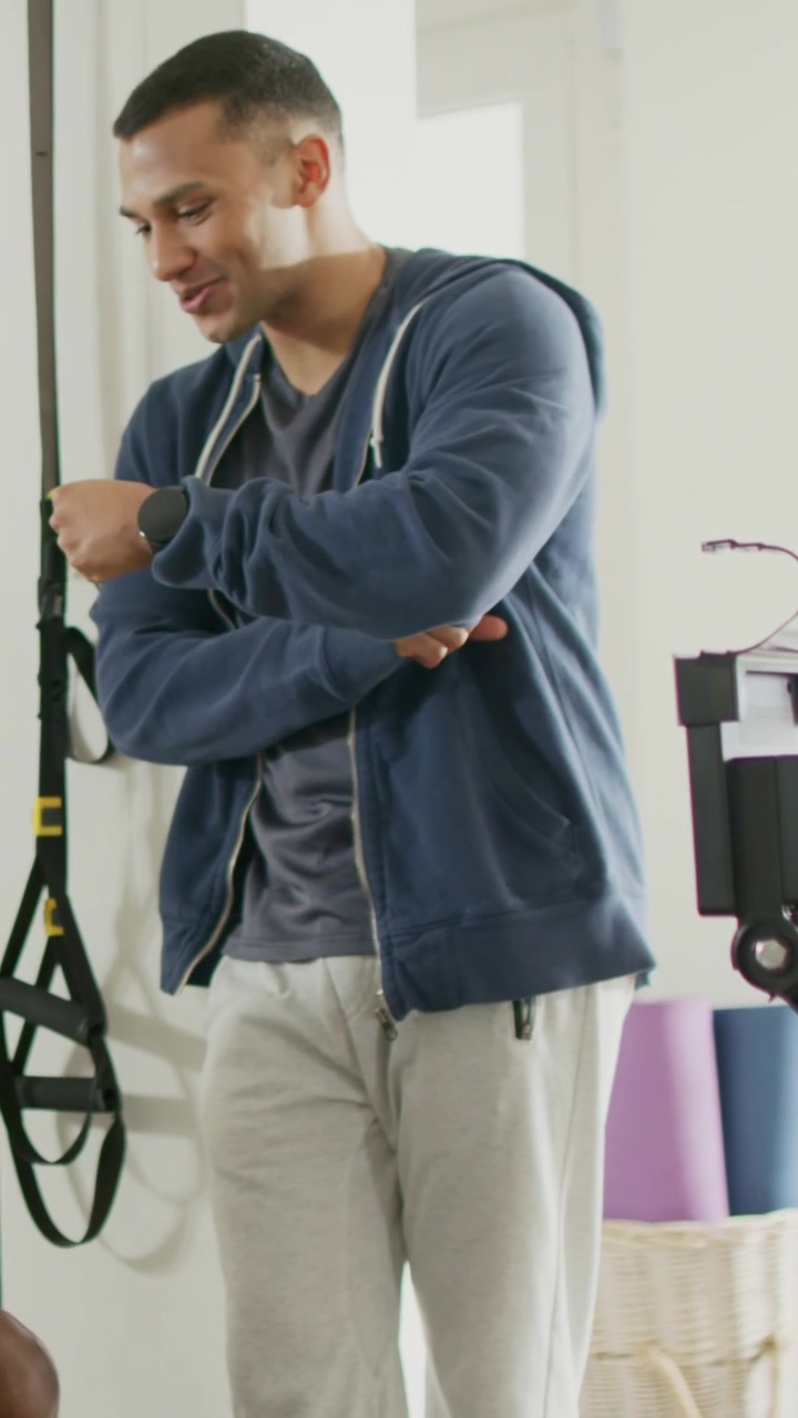 Vertical video: Leaning as hand reaching hooded man adjusting wrist checking time backing off TRX