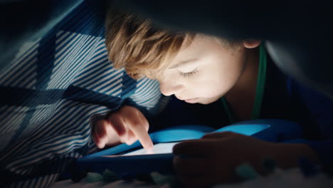 Un-Niño-Feliz-Usando-Una-Tableta-Digital-Bajo-Una-Manta-Disfrutando-Aprendiendo-Con-Tecnología-De-Pantalla-Táctil-Jugando-Juegos-Divirtiéndose-A-La-Hora-De-Dormir