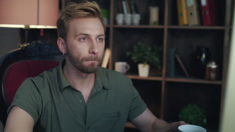 young man drinking tea and looking on computer in home office