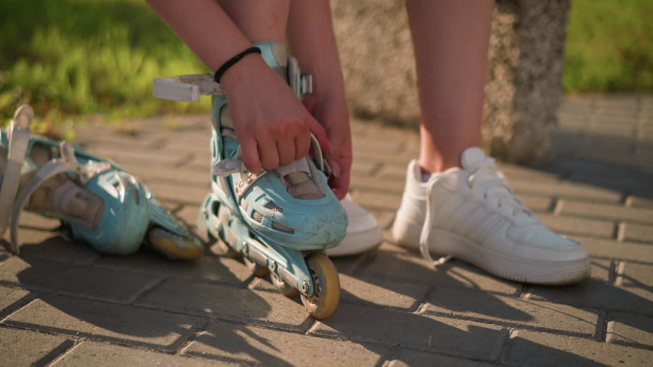 Partial view of individual adjusting roller skate strap on right leg while wearing black wristband, second roller skate is lying by in background, white sneakers placed nearby the other side