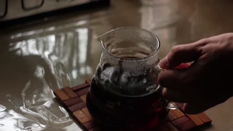hand grabbing a glass carafe and pouring brewed specialty coffee into a glass mug for drinking - close-up static shot