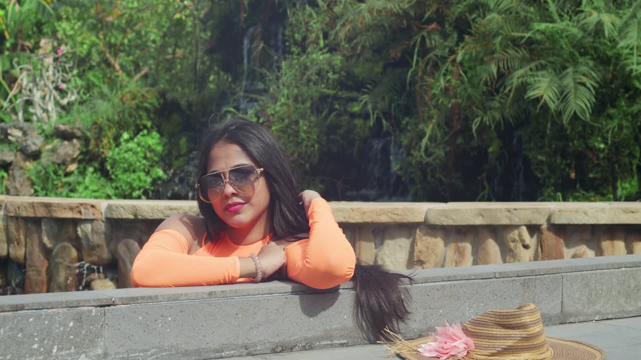 mujer en traje naranja junto a una piscina en un jardín