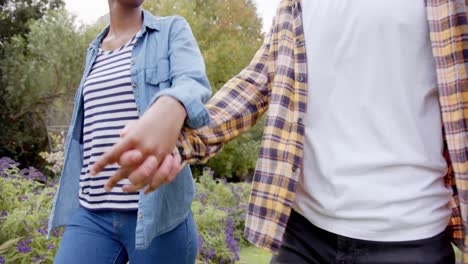 Happy-diverse-couple-holding-hands-walking-and-talking-in-garden,-slow-motion