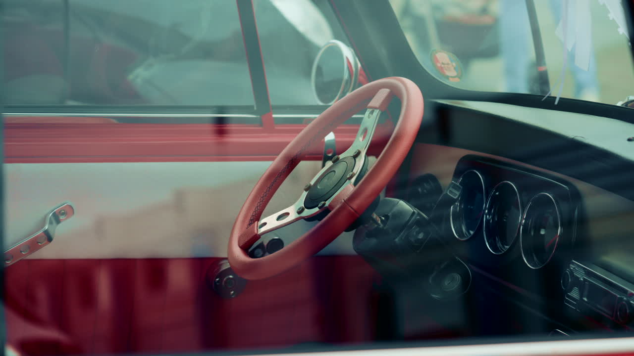 Close up of a vintage car interior shot through the window, focusing on the red steering wheel and dashboard