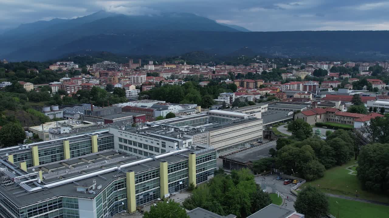 Modern glass-and-steel factory and community buildings in Ivrea's Unesco listed Olivetti district, framed by the Alps and Mount Mombarone in the background, drone shot, slow motion