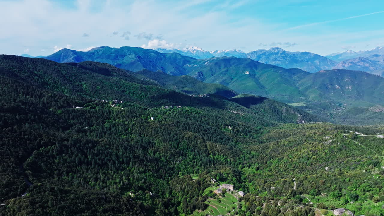 Aerial drone shot over the green lush landscape of inland Corsica, France. High view of the landscape and the mountains in the distance. Summer holidays destination for hikers and mountain lovers