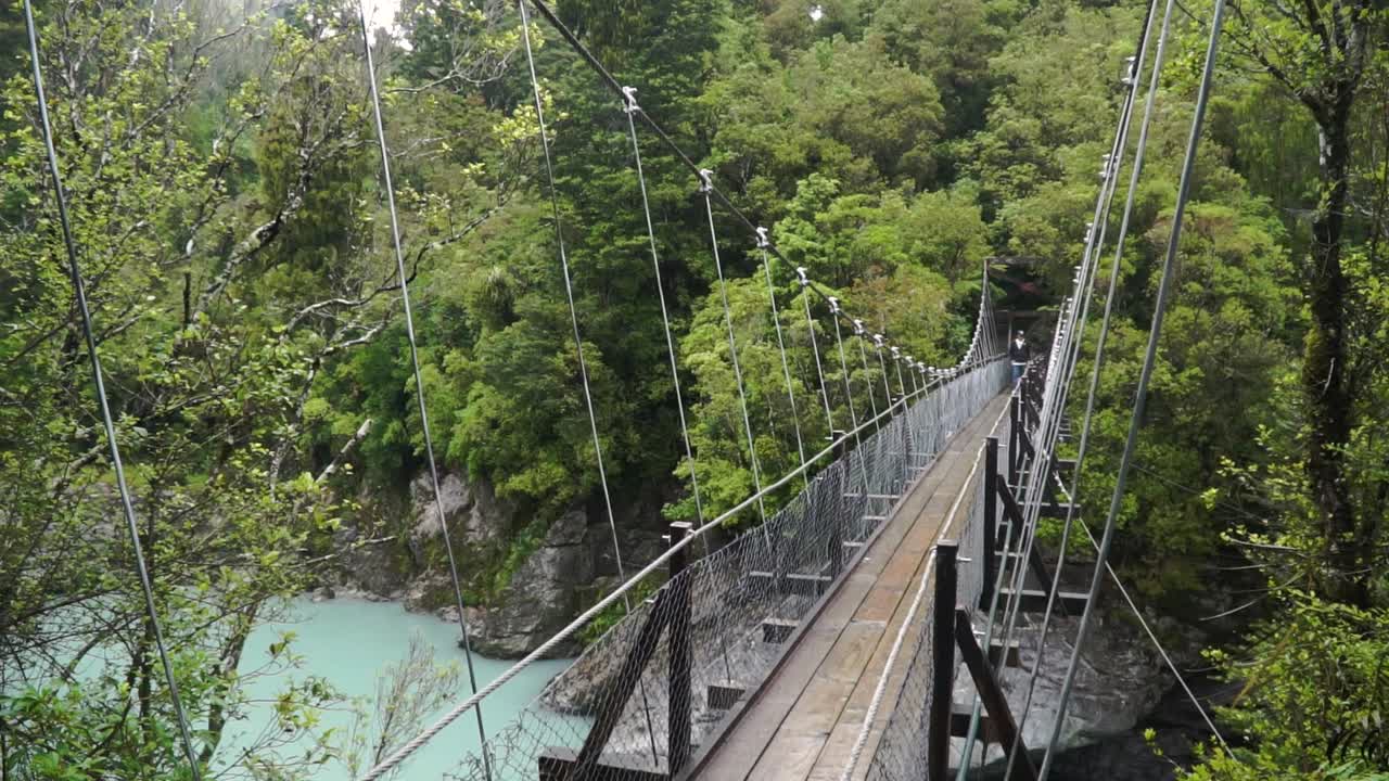 Person stands on suspension bridge over glacier river at Hokitika Gorge, New Zealand