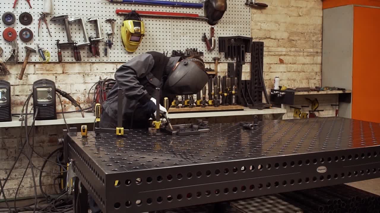 The worker is welding metal pieces in his workplace. The camera zooms in