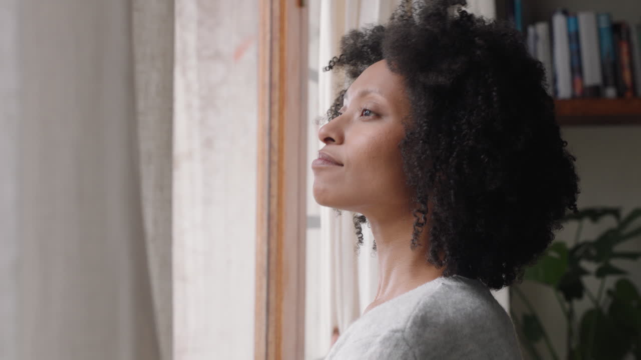 bellissima donna afroamericana che apre le tende guardando fuori dalla finestra che si allunga godendo di un nuovo giorno fresco sentendosi riposata