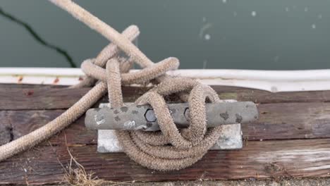 detail of a rope tied up on a bitt mounted over wooden dock