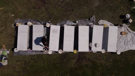 unrecognizable man paints outdoors with paintbrush seven white doors in a row