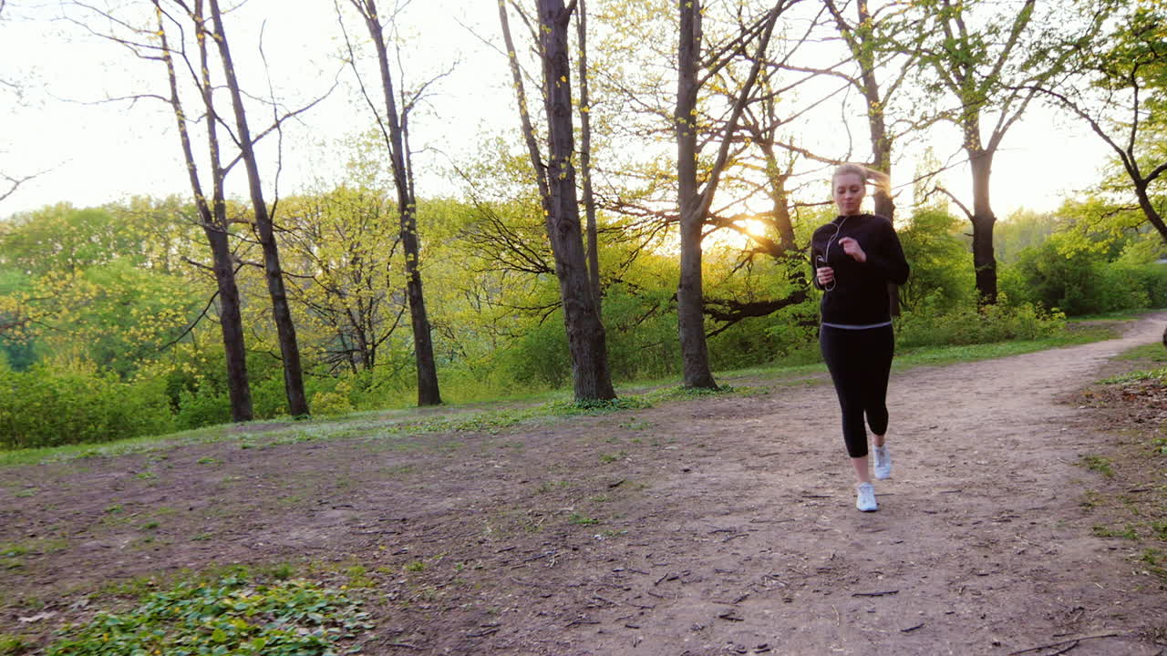 mujer joven trotando en el bosque el sol brilla maravillosamente en la cámara