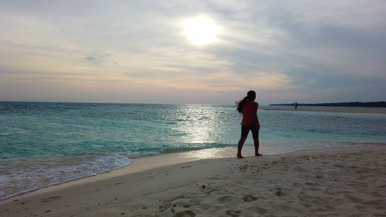 Footage of a long hair lady walking by the beach with the sunrises in the background.