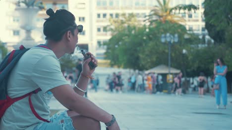 Joven-Fumando-Vape-Mientras-Está-Sentado-En-El-Parque,-Cámara-Lenta