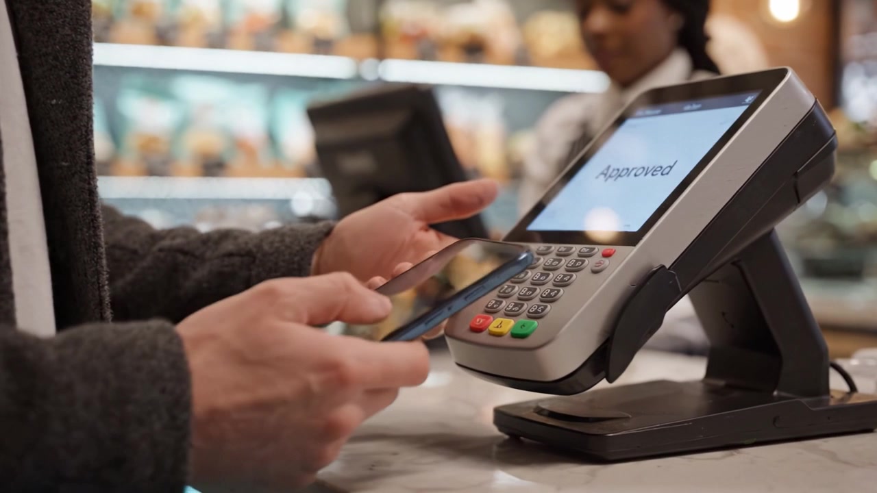 Convenient Mobile Payment at a Modern Cafe Checkout Counter with a Customer Using a Phone for Contactless Transaction and a Friendly Attendant Assisting