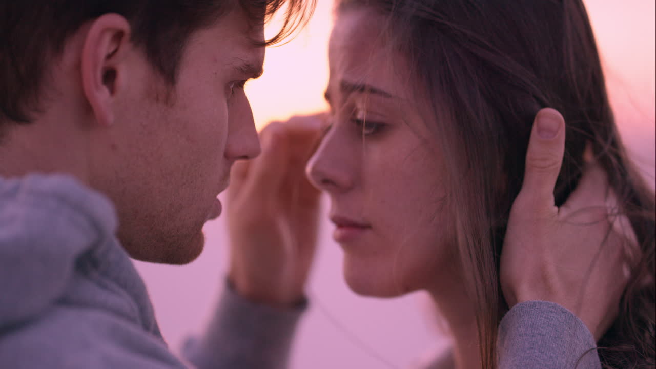 불행한 커플이 해가 지는 해변에서 화해하고 키스하고 있습니다. 슬픈 여자가 강한 잘생긴 남자에게 위로받고 있습니다.