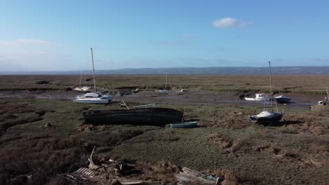 abandoned wooden fishing boat wreck shipyard in marsh mud low tide coastline aerial view dolly left