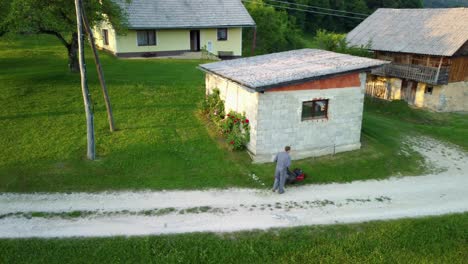 man is mowing the lawn around a small garage with red roses beside it