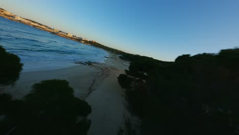 FPV-Drone-flying-close-over-trees-and-water-during-golden-hour-sunset-on-beautiful-island-and-beach