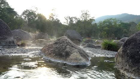 4k static shot focus shift of natural hot springs flow along the rocks under evening sunlight, the steam floating up with tree and grass background. chaeson national park, lampang,thailand.