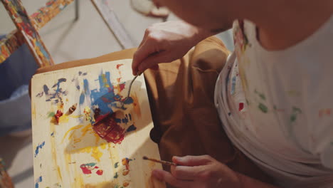 artist mixing paint colors on wooden palette