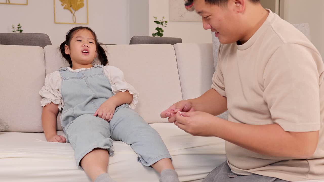 A father tends to his daughter's leg injury on a sofa in a warmly lit living room