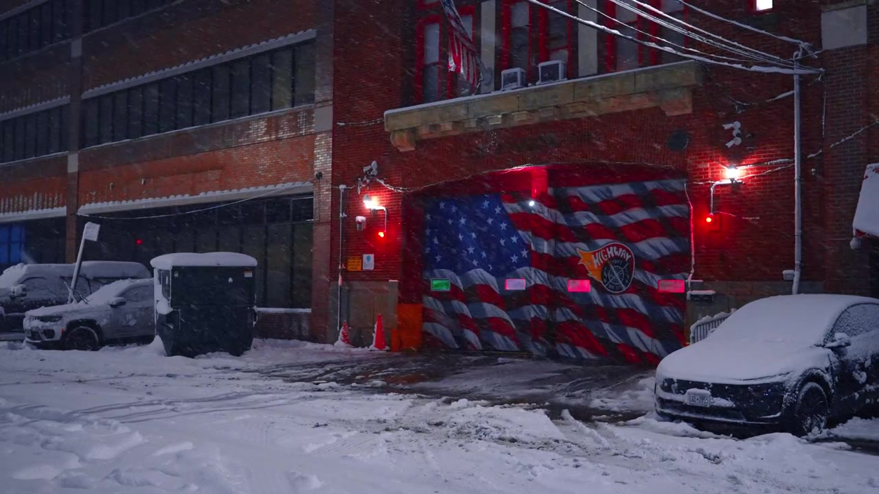 Brandstationsdøre med amerikansk flagmaleri dækket af sne. Ydersiden af en bybrandstation med et flagmaleri og røde lys under en vinterstorm i NYC.